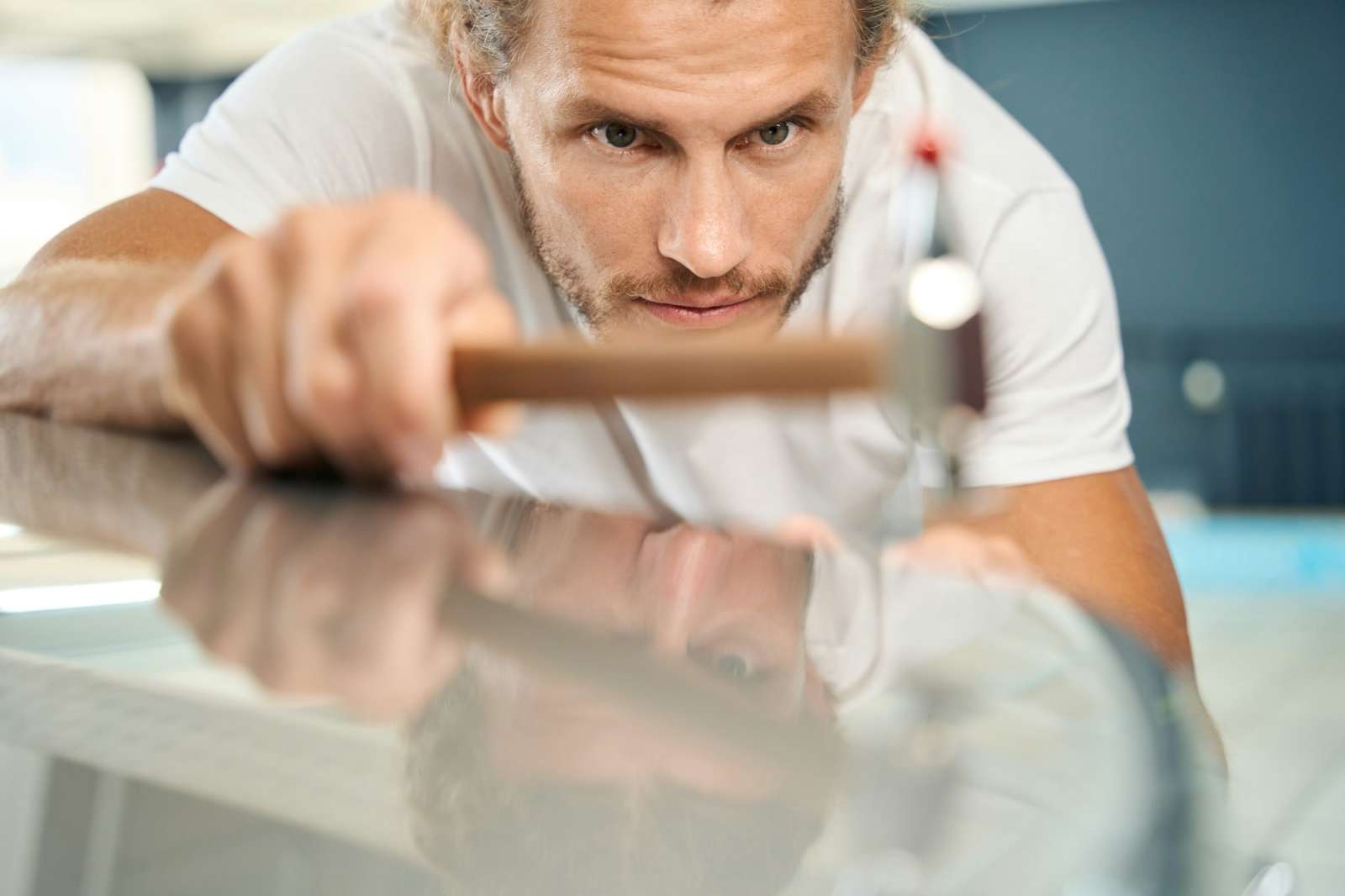 Unshaven man straightens body of white car with straightening hammer