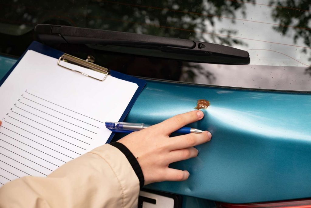 Car damage inspection with clipboard and pen on a blue car's dented surface.